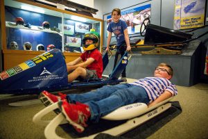 Three young boys with a bobsled and luge in the Lake Placid Olympic Museum