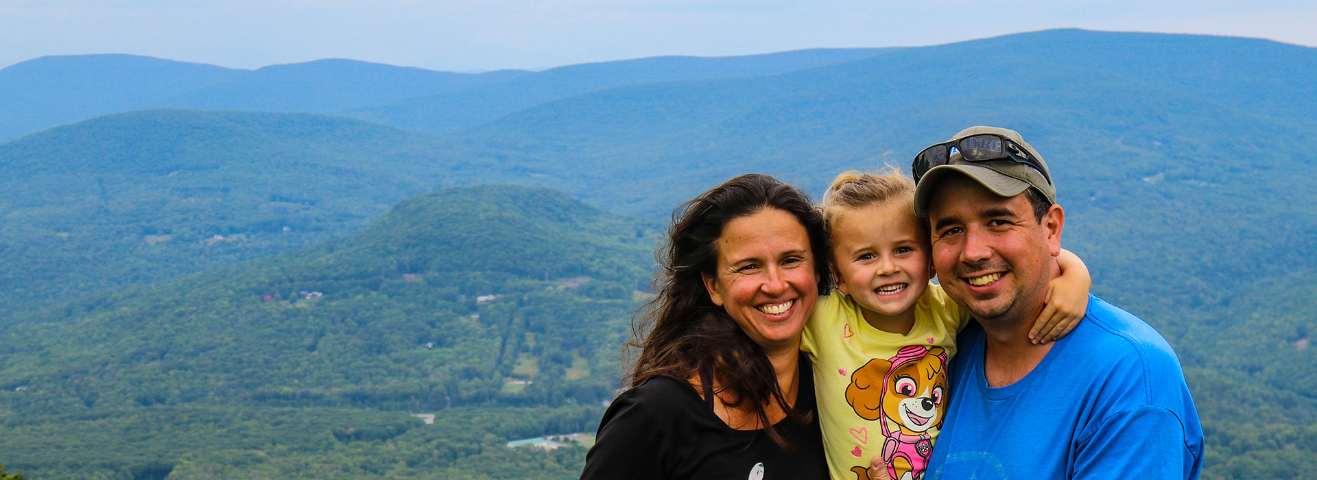 A family with all smiles at the summit of Belleayre Mountain with the green landscape as a backdrop