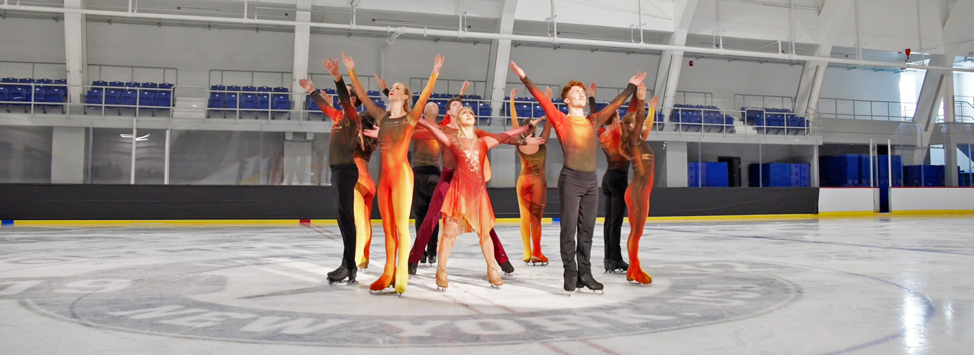 Performers in colorful wardrobe stand at center ice with their arms in the air at the end of their performance in the 1932 Jack Shea Arena.
