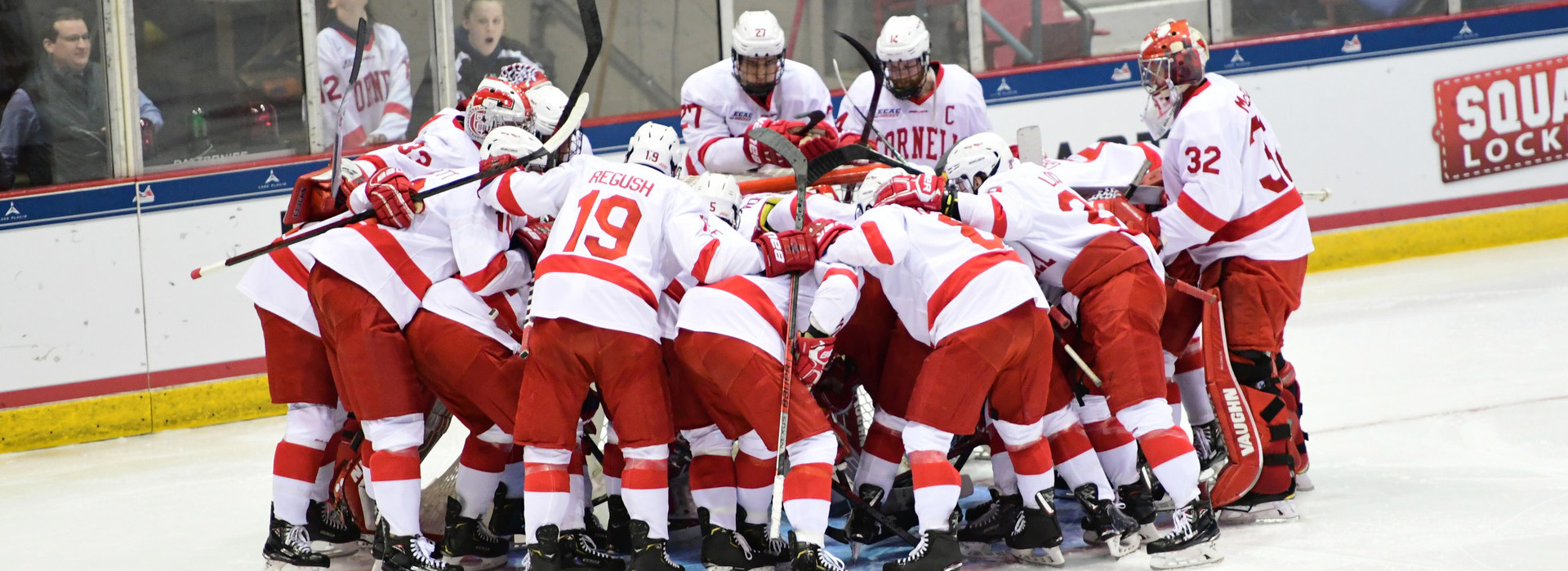 The Cornell men's ice hockey team in red and white uniforms huddles on the ice with arms around one another at the 2019 ECAC Championships.
