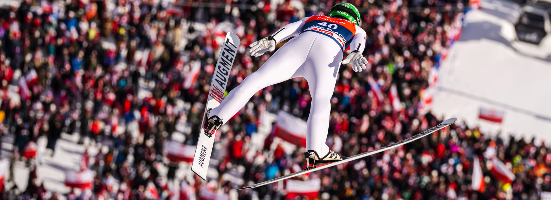 Ski jumper soars through the air over a massive crowd below.