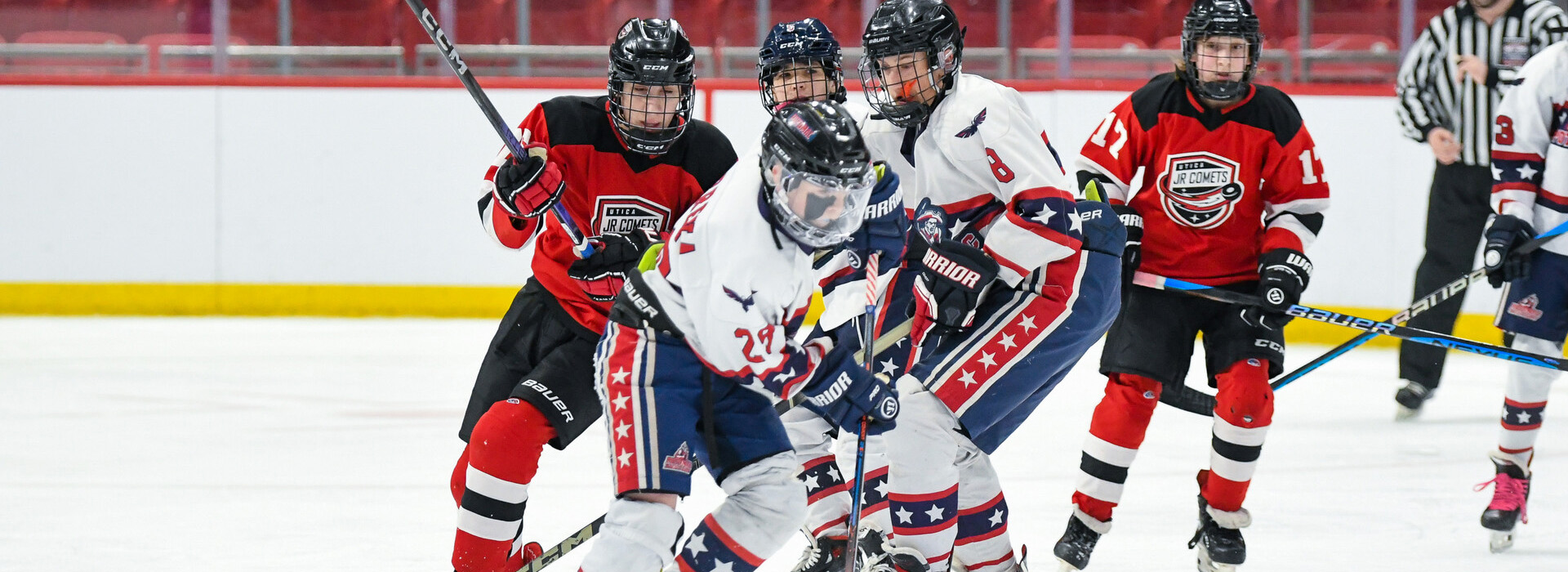 A group of several teen hockey players from opposing teams battle for the puck on the ice in the 1980 Rink.