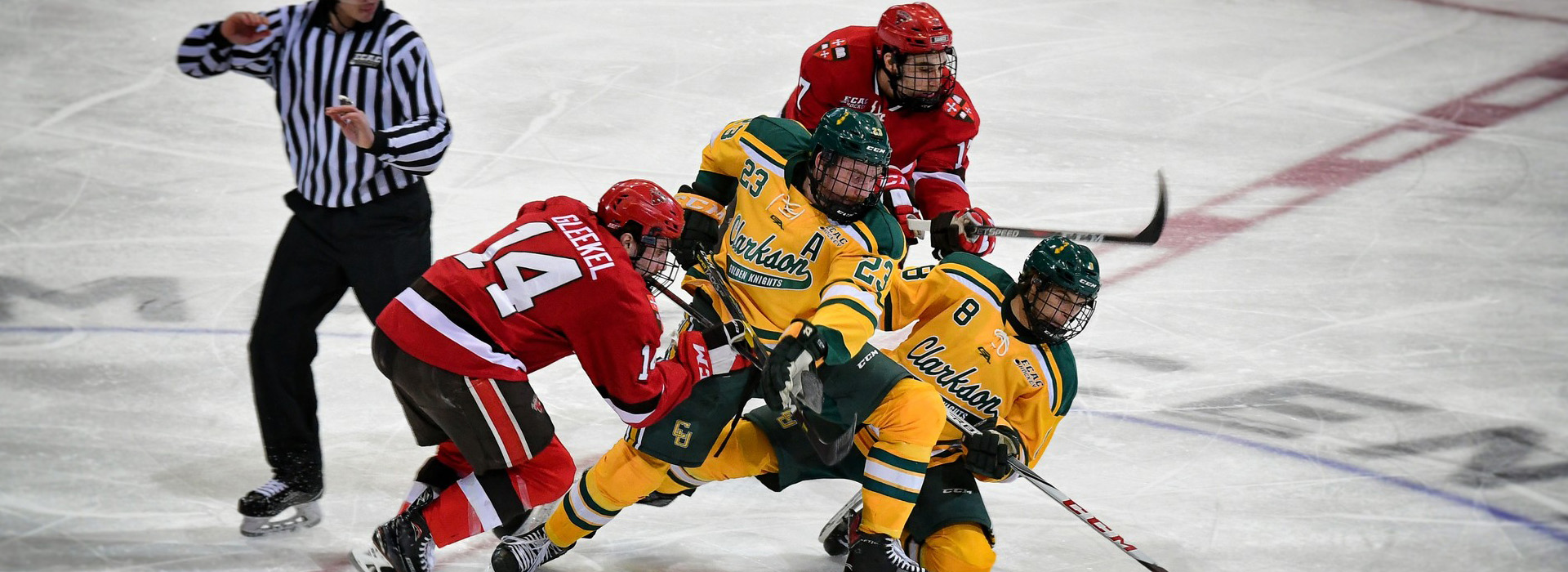 Four men, two from each of two teams, battle for the puck at center ice with a referee scrambling to get out of the way.
