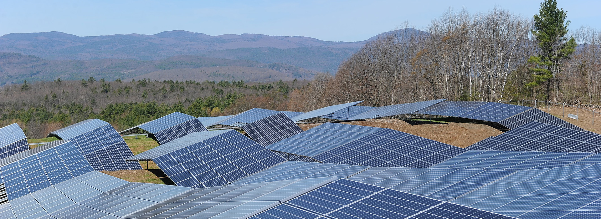 A large solar array with mountains and blue sky in the background.