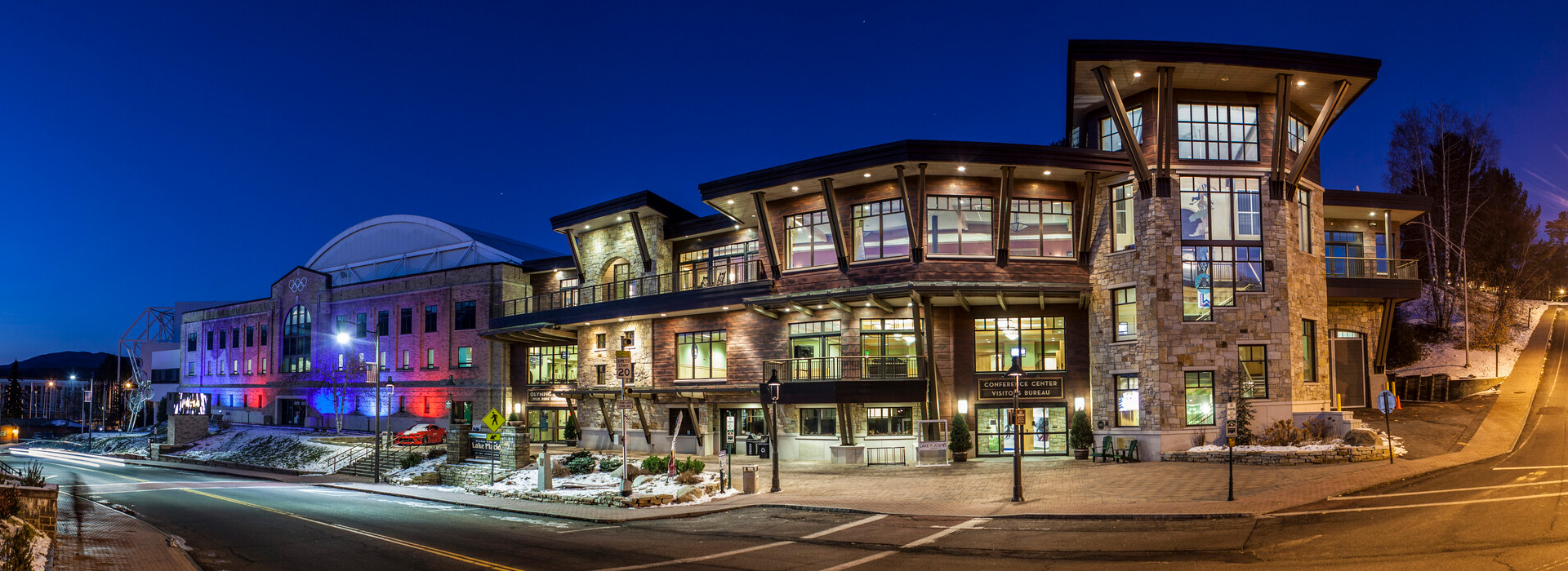 The Lake Placid Conference Center and 1932 Olympic Center entrance at night with lights n all windows and a deep blue sky above with the street in front.