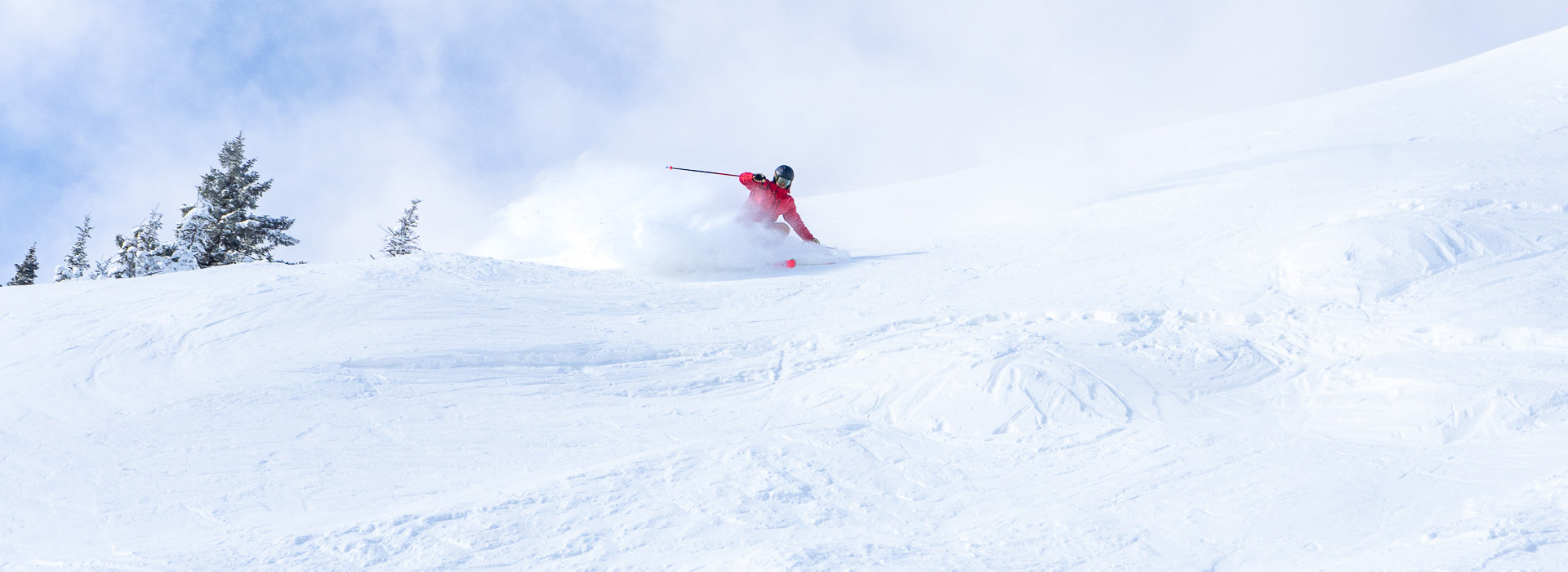 A skier in red with a black helmet makes a hard turn on packed powder high on Gore Mountain.