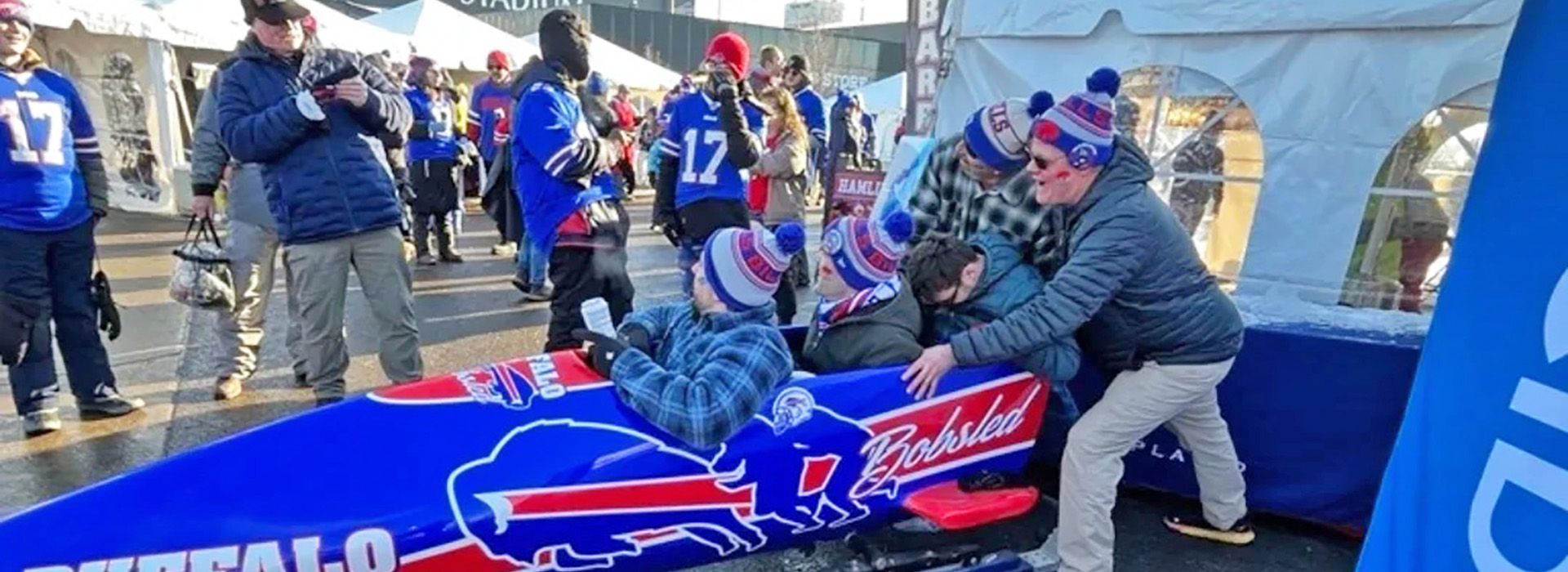The buffalo bobsled parked at High Mark Stadium with fans inside the sled and John Morgan outside taking their photo.