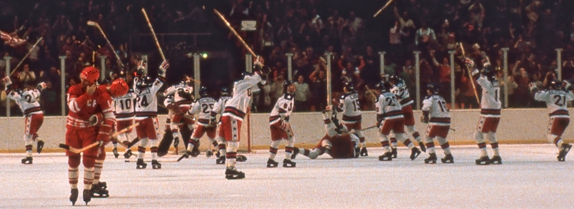 The conclusion of the Miracle on Ice Game at the Lake Placid Olympic Center with Team USA celebrating amidst the Russian players still on the ice with the crowd cheering in the background.