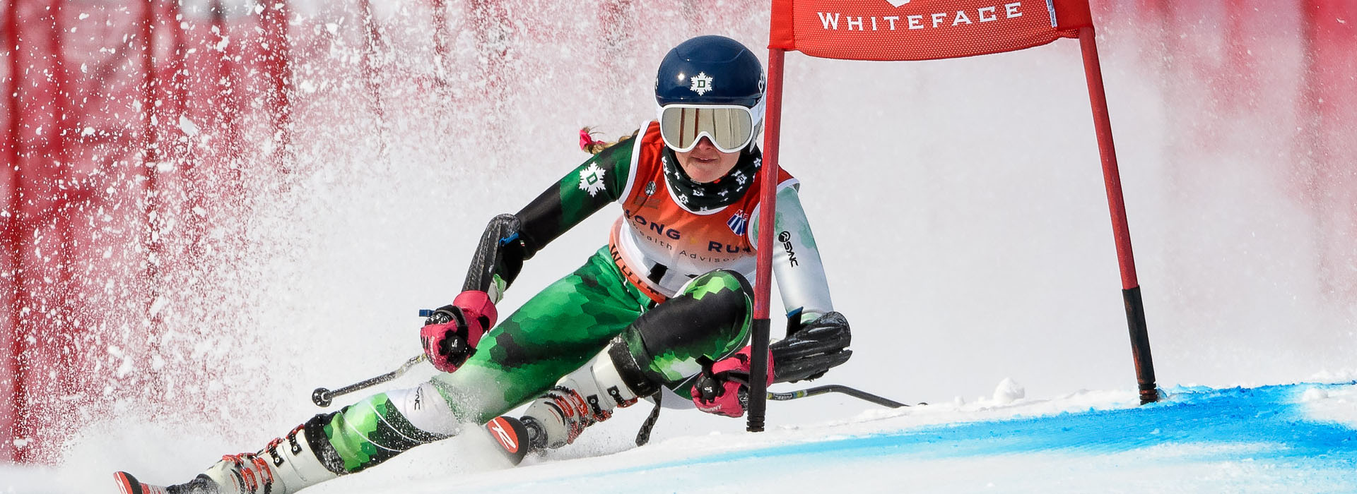 A female ski racer turning hard and fast around a red gate.