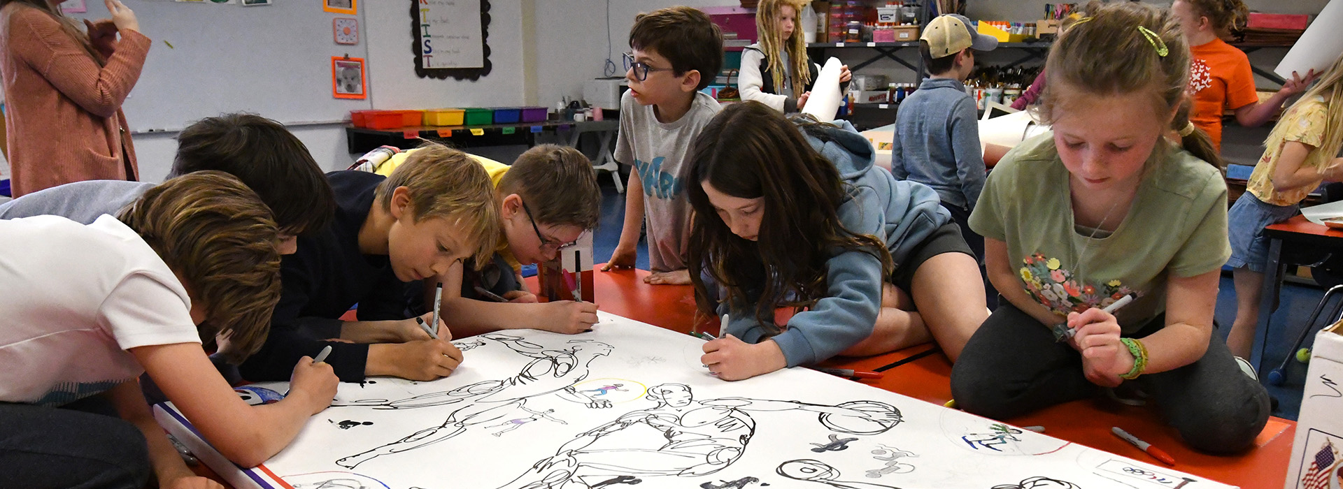 A group of children work on an art project together coloring in a black and white outline in a classroom.