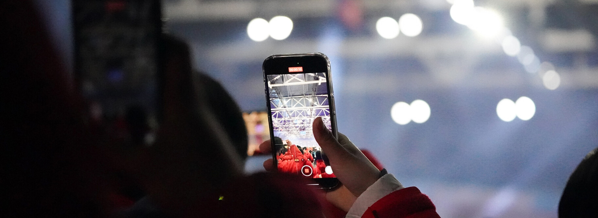 A spectator at opening ceremonies holds up his phone to take photos with globe lights in the background.