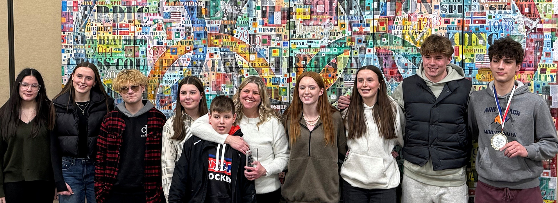 Some of the Art of the Olympians contest winners line up for a portrait in front of an artwork produced by the region's youth.