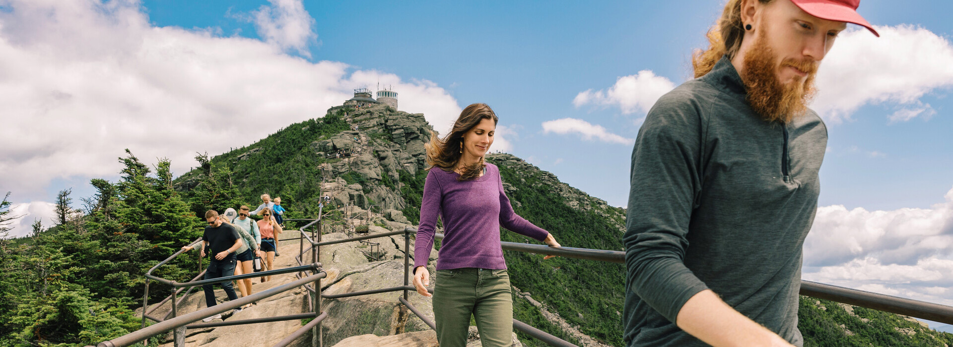 A young woman hikes down the trail from the Whiteface Summit with a young man a few paces in front of her.