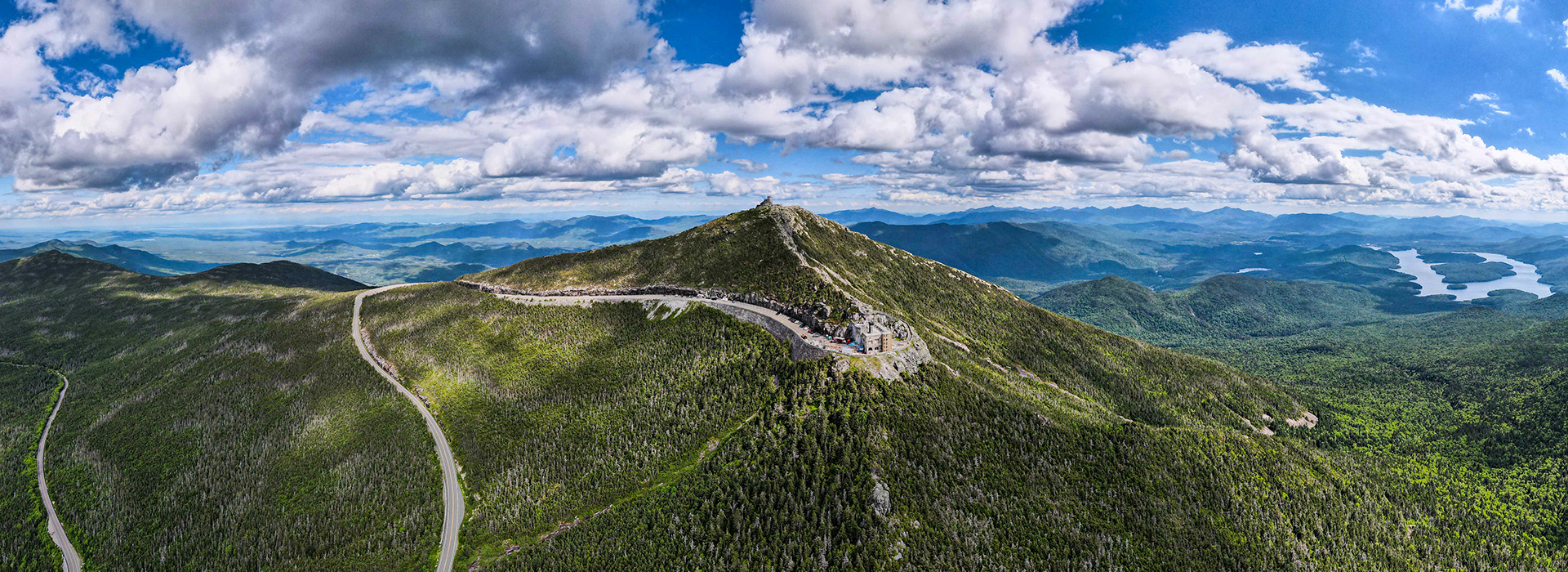 Panoramic view of Whiteface Mountain and the Veterans' Memorial Highway in summer with puffy clouds in the sky.