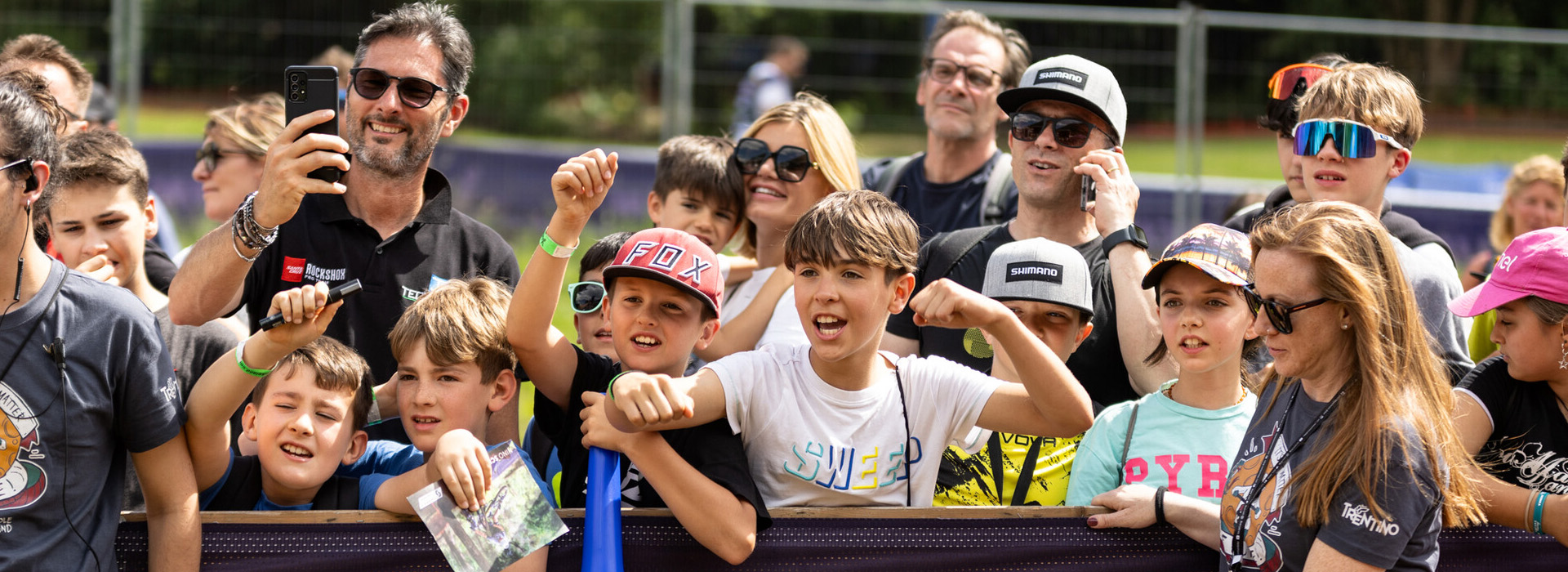 Young spectators and adults alongside the race course cheering for the UCI Mountain Bike World Series riders.