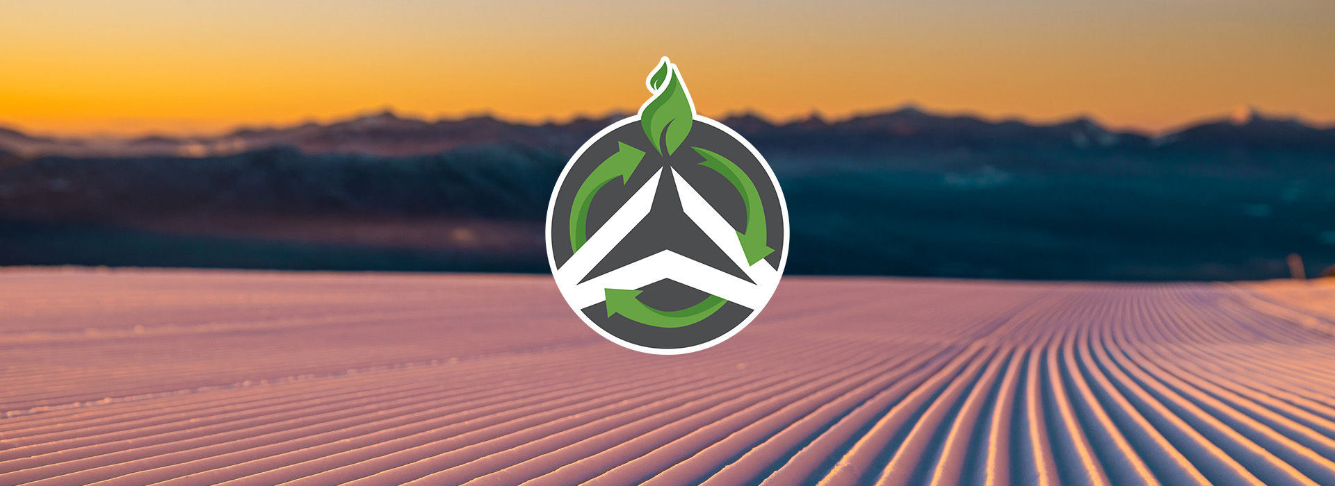 Freshly groomed snow in the foreground in focus with mountains out of focus in the background and in the center the Olympic Authority sustainability logo with green recycling arrows circling the standard corporate logo.