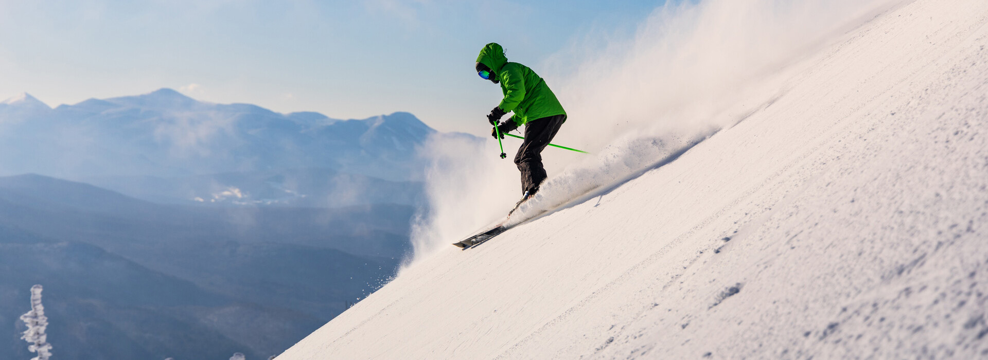 Skier in a green jacket skis a steep slope with beautiful mountain vistas in the background.