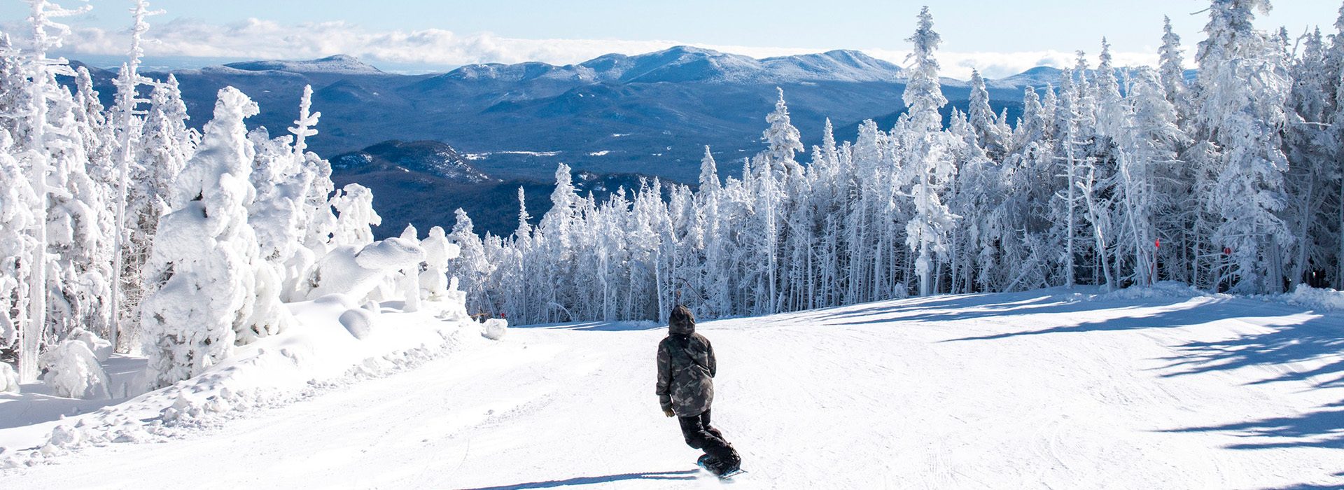 A snowboarder rides the Approach run on a clear winter day with beautiful views ahead of him.
