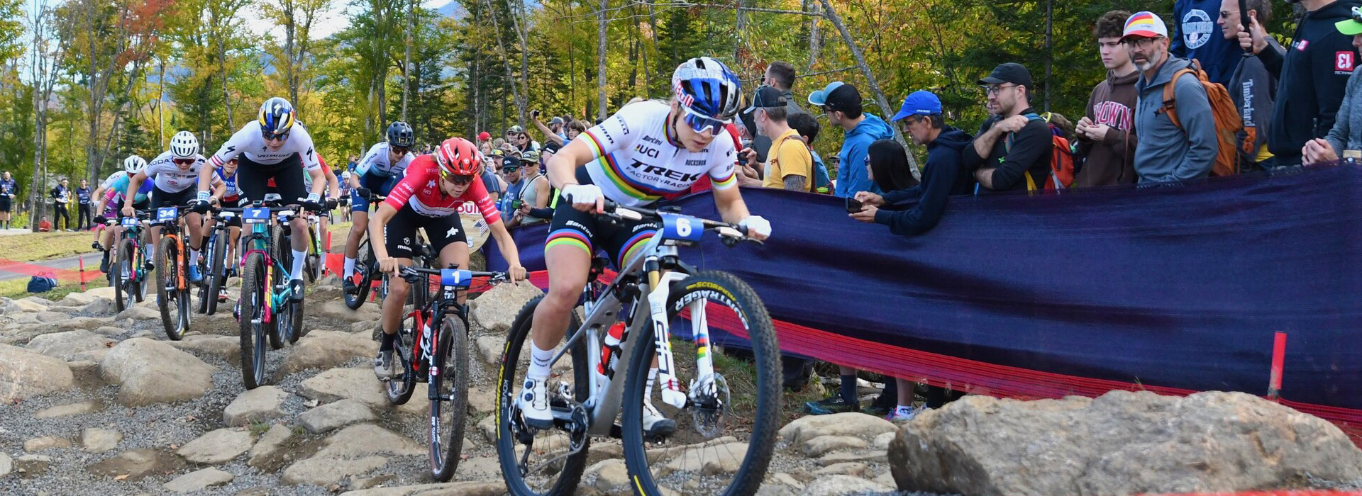Female UKCI riders in a rock garden at Mt Van Hoevenberg with spectators looking on just a few feet away.