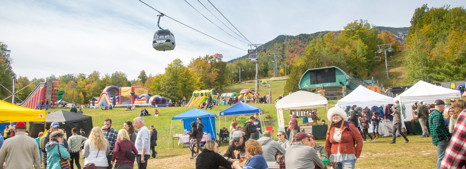 People enjoy Oktoberfest at Whiteface whiile the gondola goes overhead against the backdrop of fall leaves on the mountain.