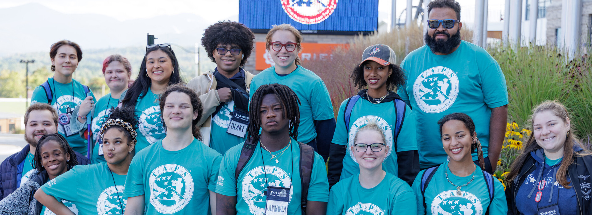 About a dozen members of the TAPS youth group in matching TAPS t-shirts standing together outside the Olympic Center.