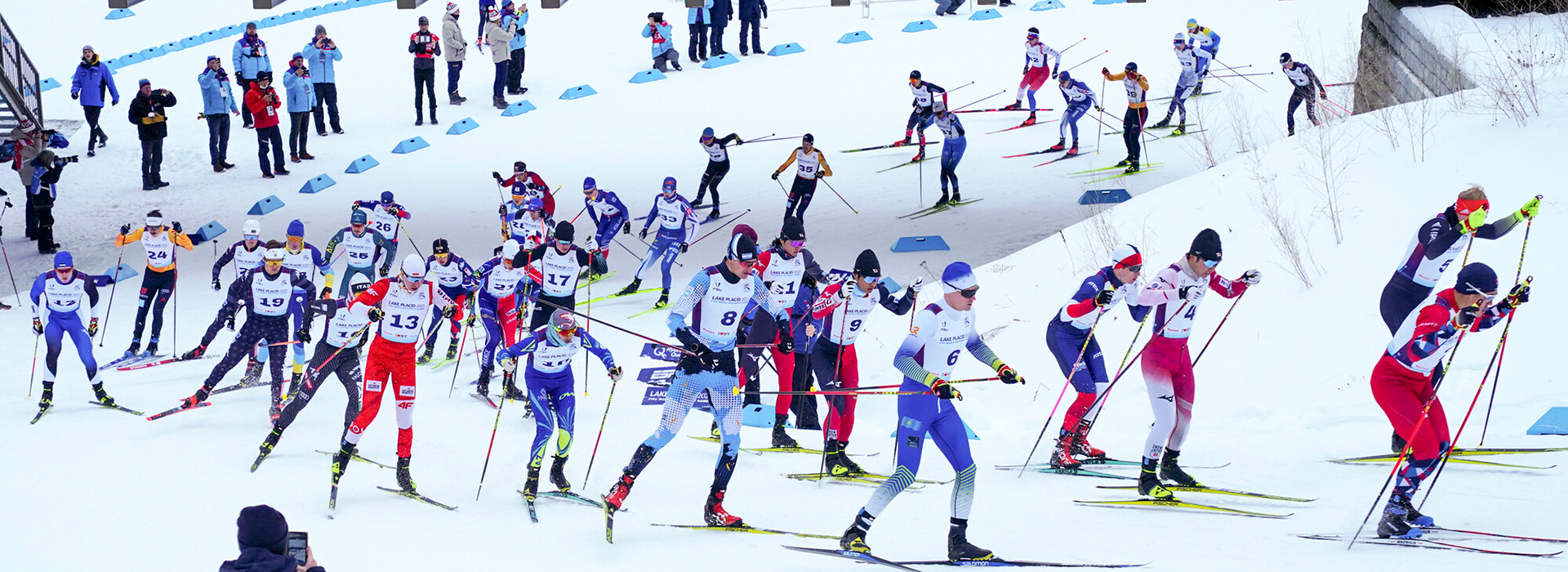 Many cross-country ski racers round a corner down a hill during a race at Mt Van Hoevenberg.
