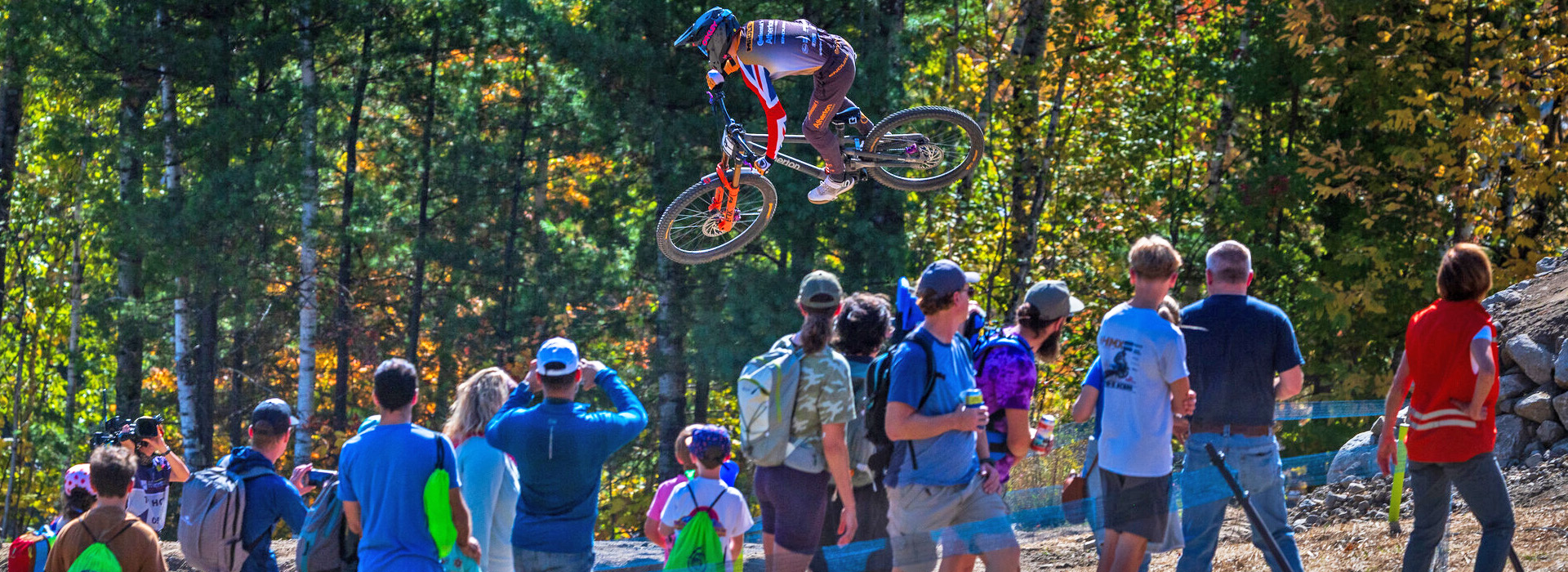 A downhill mtb competitor flies through the air next to a group of spectators on Whiteface Mountain.