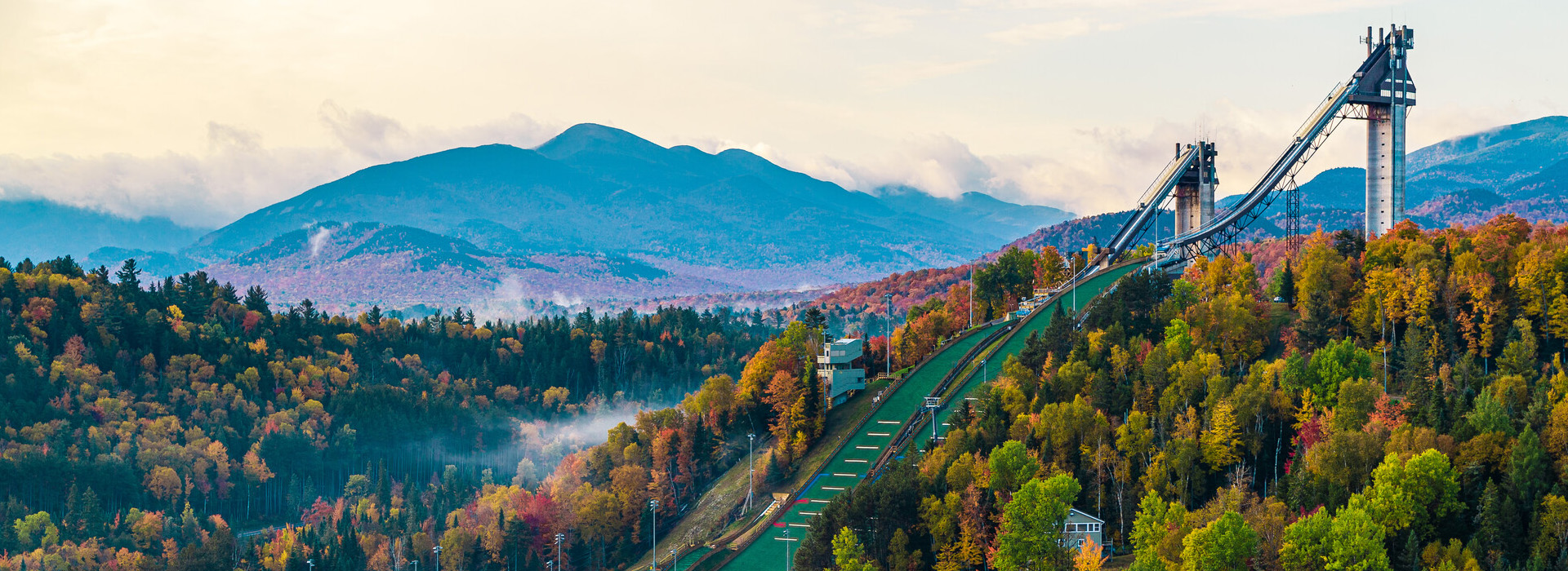 Image of the Olympic Jumping Complex big jumps among a fall landscape with the Adirondack High Peaks in the background.