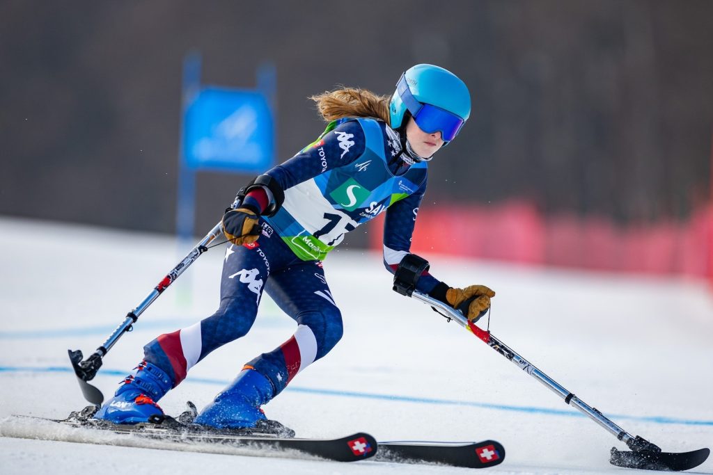 Kelsey racing hard wearing a blue uniform with a gate and red fence tin the background.