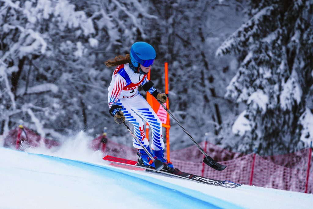 Kelsey racing hard in a white Team USA uniform with trees in the background.