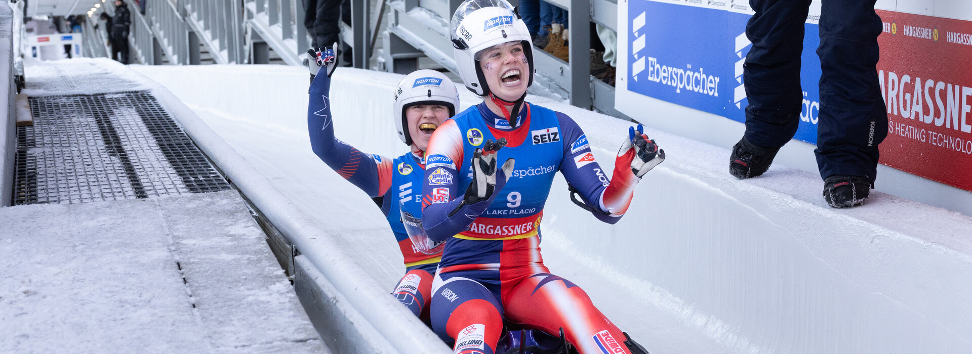 Female luge athletes Sophie Kirkby and Chevonne Forgan come the finish race finish area cheering and smiling.