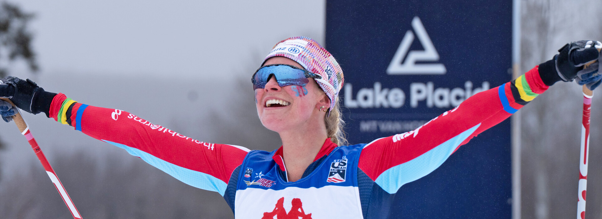 A close up of Jessie Diggins at Mt Van Hoevenberg, smiling with her arms outstretched after completing a race.