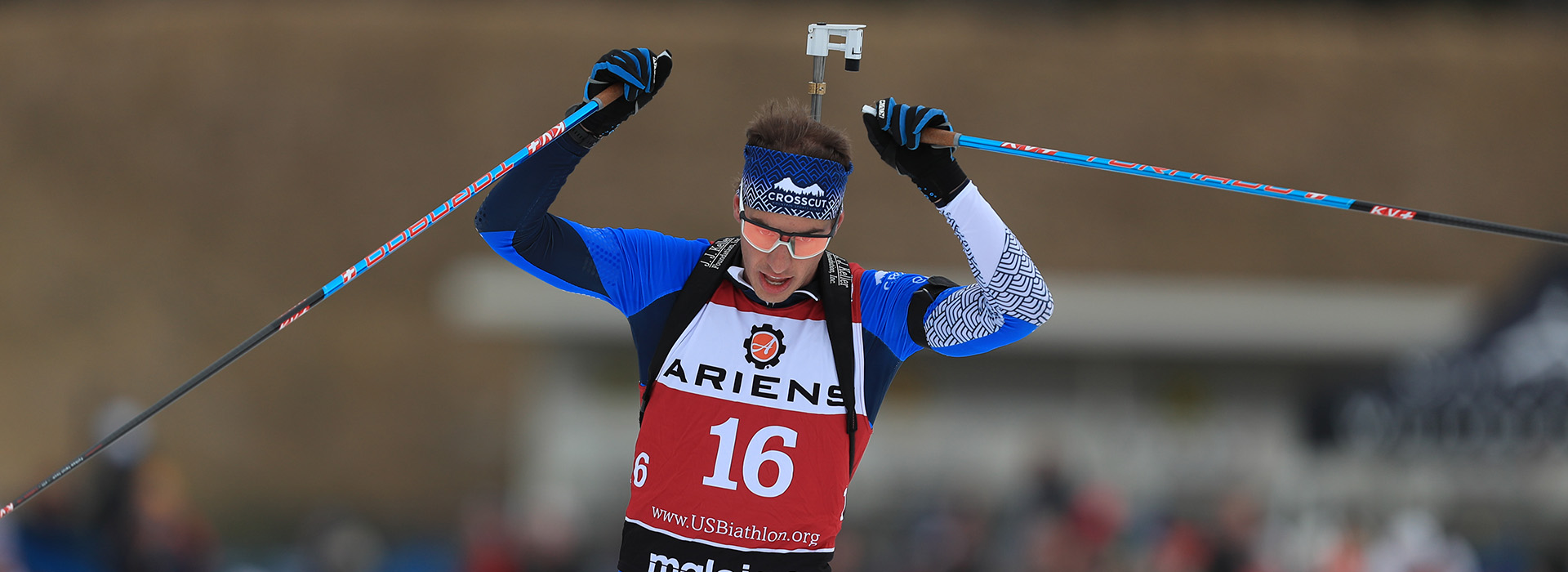 A male biathlete raises his hands in triumph as he crosses the finish line.