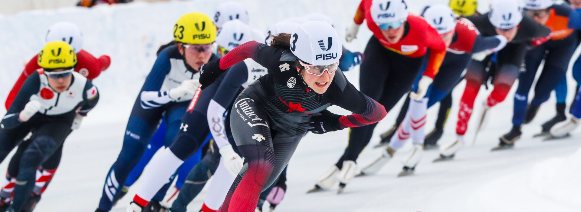 A line of women speed skaters skating fast and competing in a race in the 2023 FISU Games in Lake Placid.