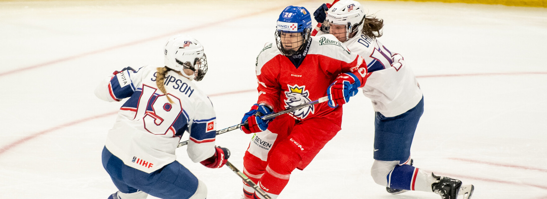 Three women hockey players battle for position and the puck on the ice in the 1980 Herb Brooks Arena.