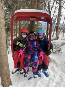 Three young Johnsburg students sitting and smiling in an antique red lift chair.