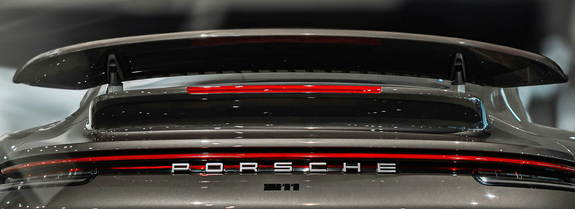 Rear end of a grey Porsche car showing the brand name and the spoiler on the back.