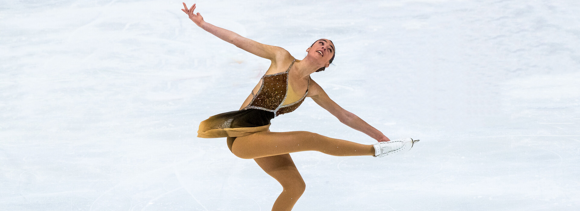 Female figure skater spins with her arms outstreached and one leg raised with ice all around her.
