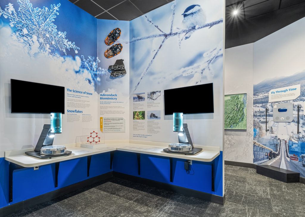 An interactive display titled "the Science of Snow" with two large monitors for viewing and microscopes for visitors to look into.