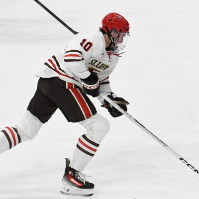 A St. Lawrence University hockey player in a white jersey and red helmet handles the puck as he breaks away down the ice.