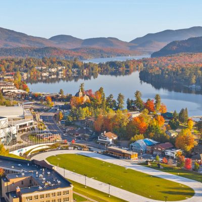 The Olympic Center viewed from high above in Autumn with the Village of Lake Placid, Mirror Lake, and mountains in the background.
