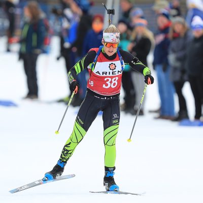 A female biathlete skis in front of a crowd at Mt Van Hoevenberg.