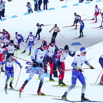 Many cross-country ski racers round a corner down a hill during a race at Mt Van Hoevenberg.