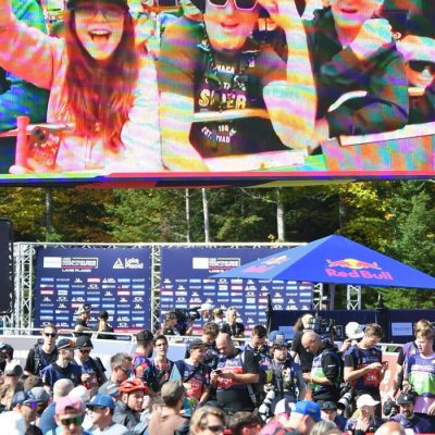 The start area at the UCI World Series at Mt Van Hoevenberg with large screen TVs and images of spectators above and fans mingling below.