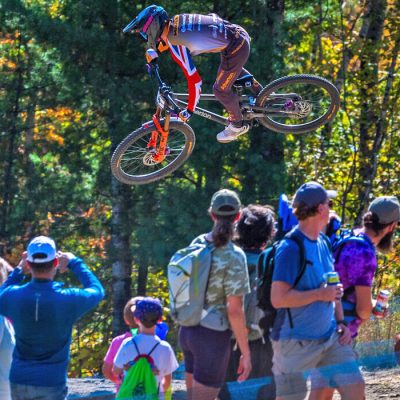 A downhill mtb competitor flies through the air next to a group of spectators on Whiteface Mountain.