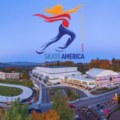 An aerial photo of the Lake Placid Olympic Center on a fall day with a blue sky and the Skate America logo above the Olympic Center.