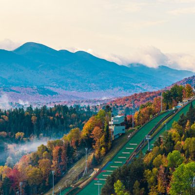 Image of the Olympic Jumping Complex big jumps among a fall landscape with the Adirondack High Peaks in the background.