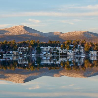 Downtown Lake Placid on a winters day as seen from across Mirror Lake before the lake is frozen with a beautiful reflection of the entire scene.