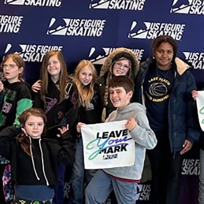 A large group of area youth pose with "Leave Your Mark" signs standing in front of a Saatva Skate America background.