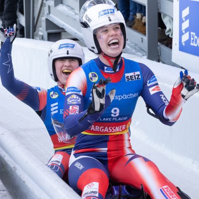Female luge athletes Sophie Kirkby and Chevonne Forgan come the finish race finish area cheering and smiling.